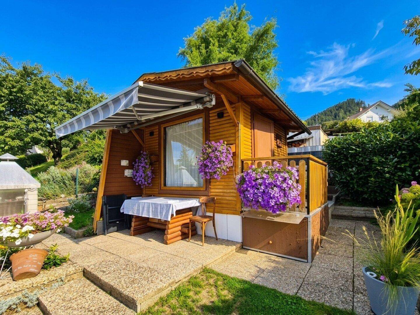 Charmantes Holzhaus im Garten mit Markise, Esstisch im Freien und üppiger Blumendekoration.