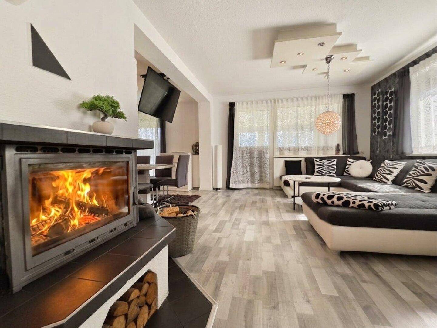 Geräumiges Wohnzimmer mit großem Ecksofa, gemütlichem Kamin und Fenstern mit Vorhängen.