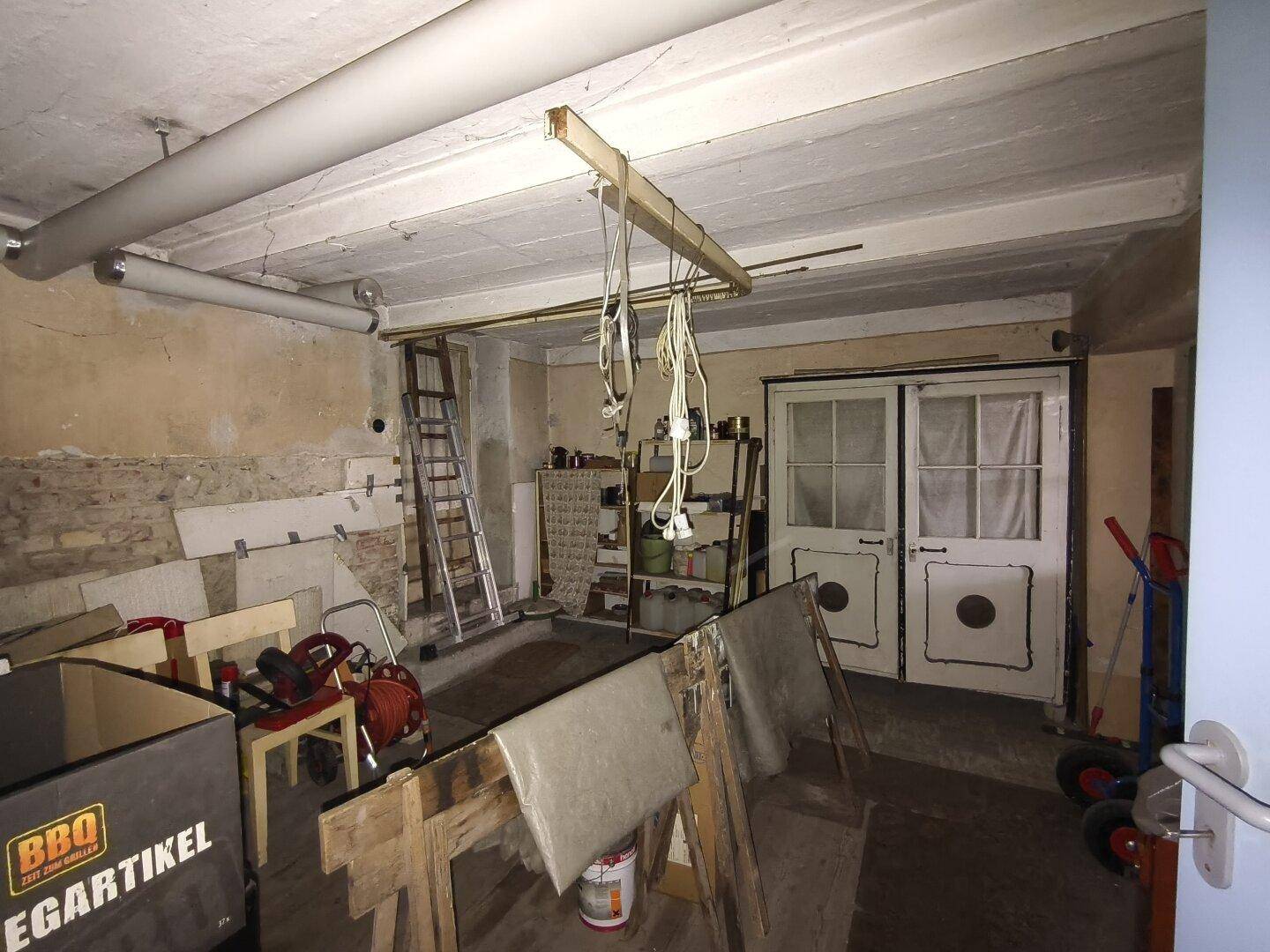 Unausgebauter Kellerraum mit Lagerflächen, Werkzeugen und doppelten Holztüren.