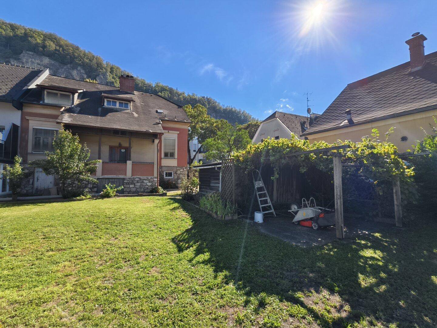 Garten mit überdachtem Bereich, Rasenfläche und Blick auf das historische Wohnhaus.