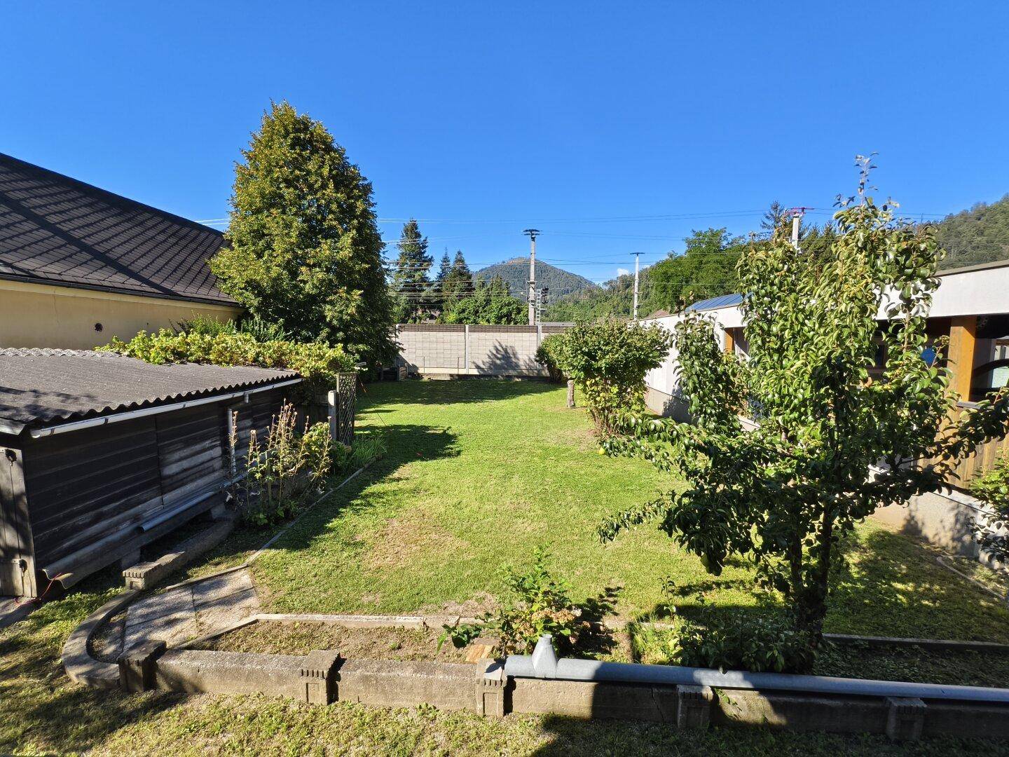Garten mit Obstbäumen und Rasenfläche, umgeben von einer Mauer und grüner Landschaft.