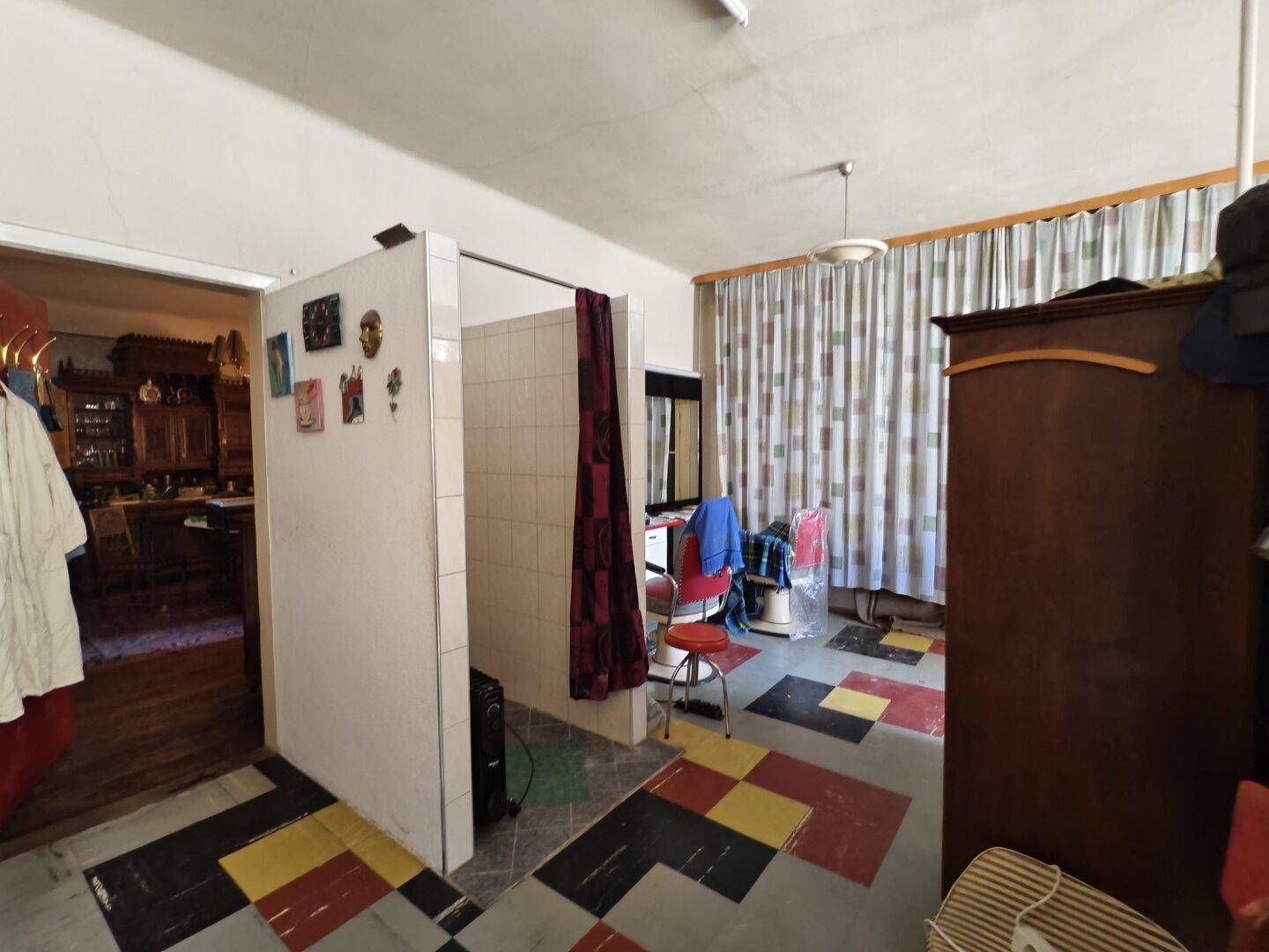Raum mit integriertem Duschbereich, farbigen Bodenfliesen und Zugang zu einem weiteren Zimmer.