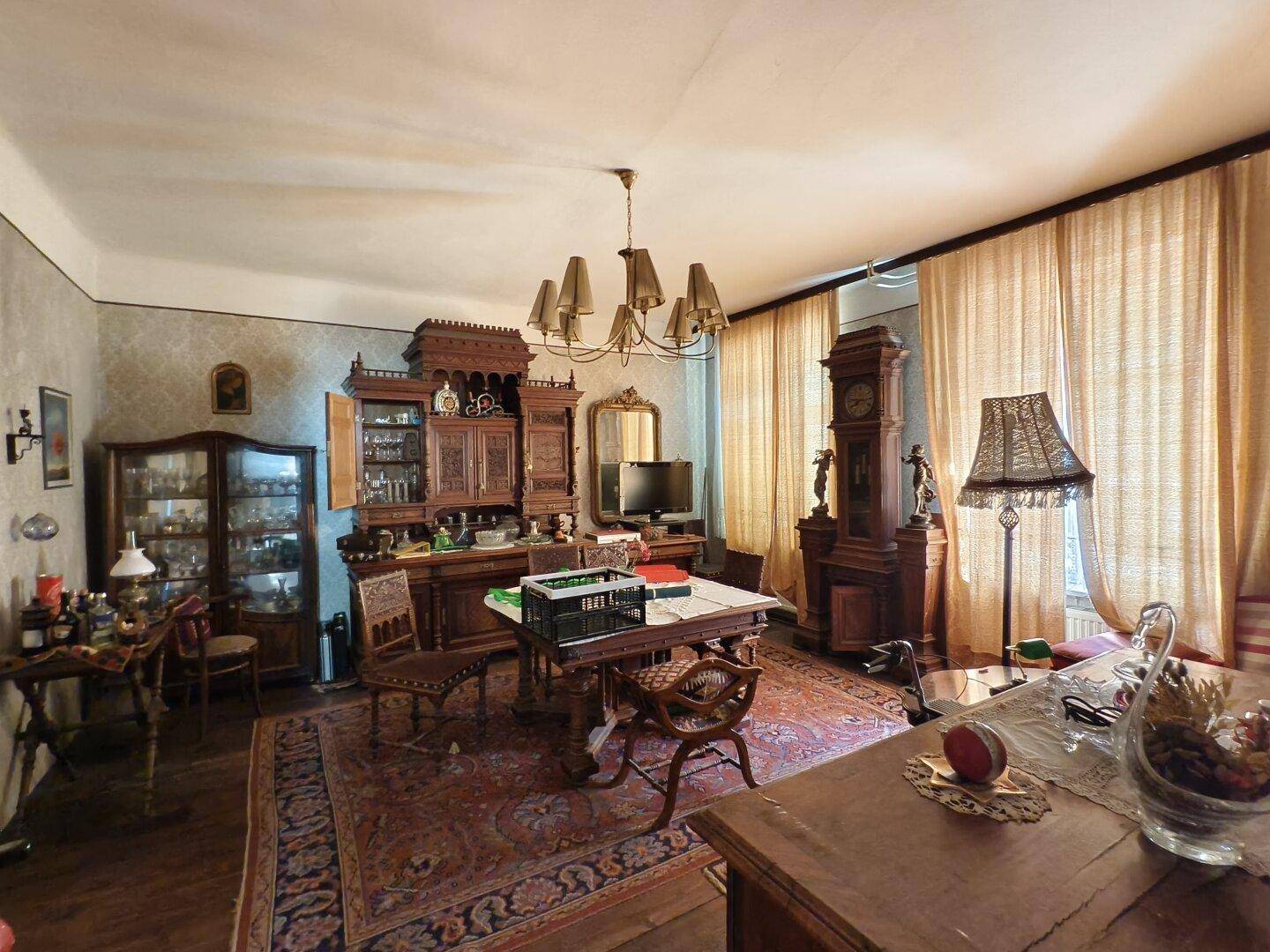 Traditionelles Wohnzimmer mit antiken Holzmöbeln, Teppichboden und schweren Vorhängen.