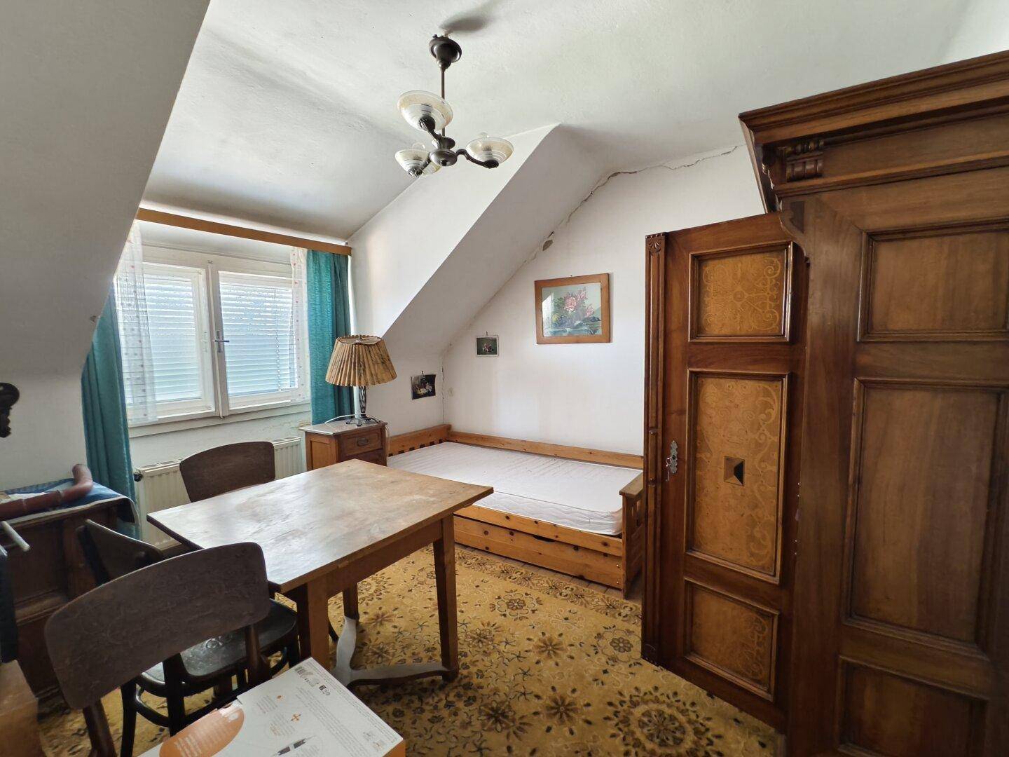 Dachschlafzimmer mit schräger Decke, Holzboden und einfacher Einrichtung.