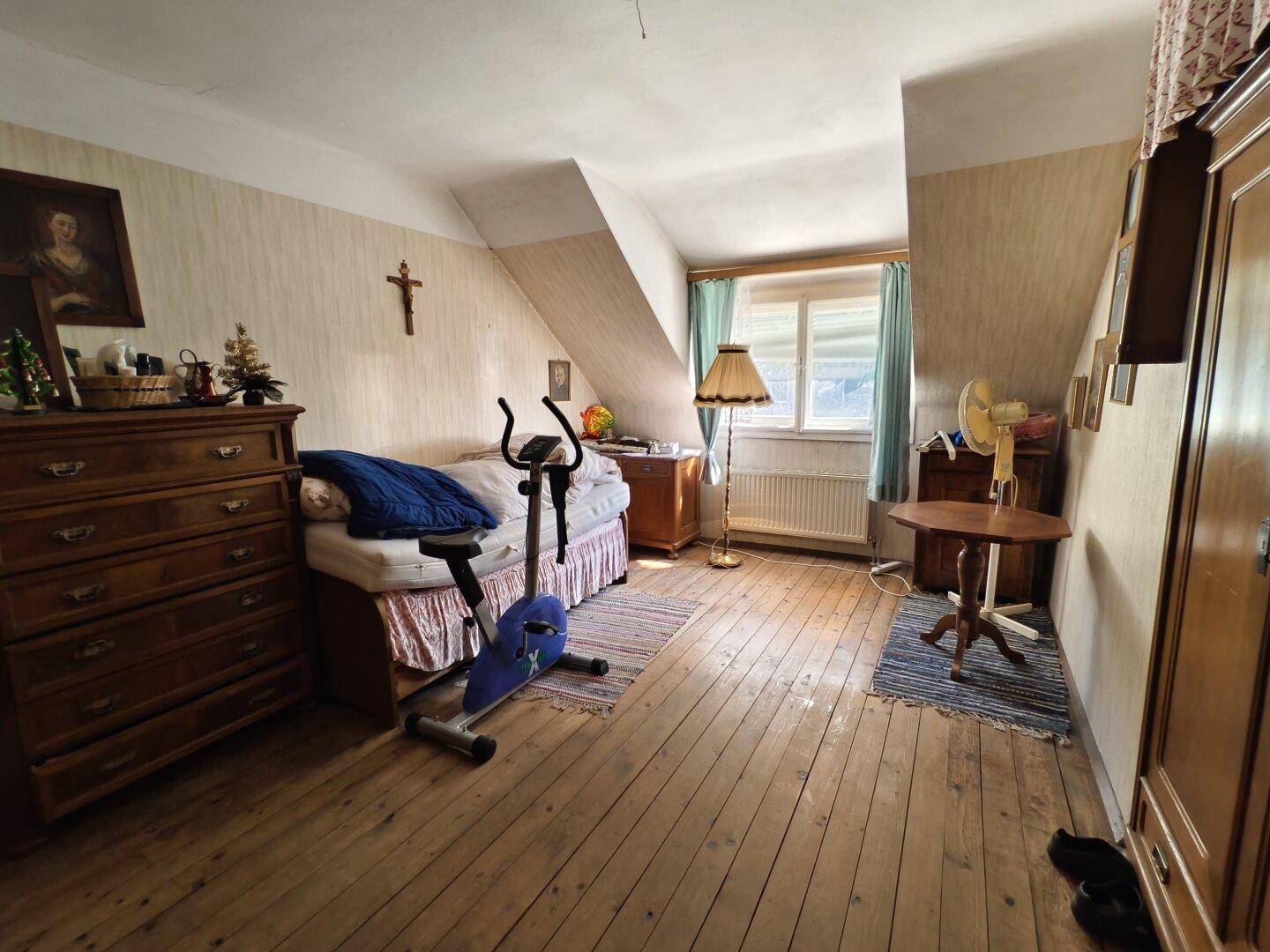 Dachzimmer mit Holzdielenboden, schräger Decke und einem Heimtrainer.
