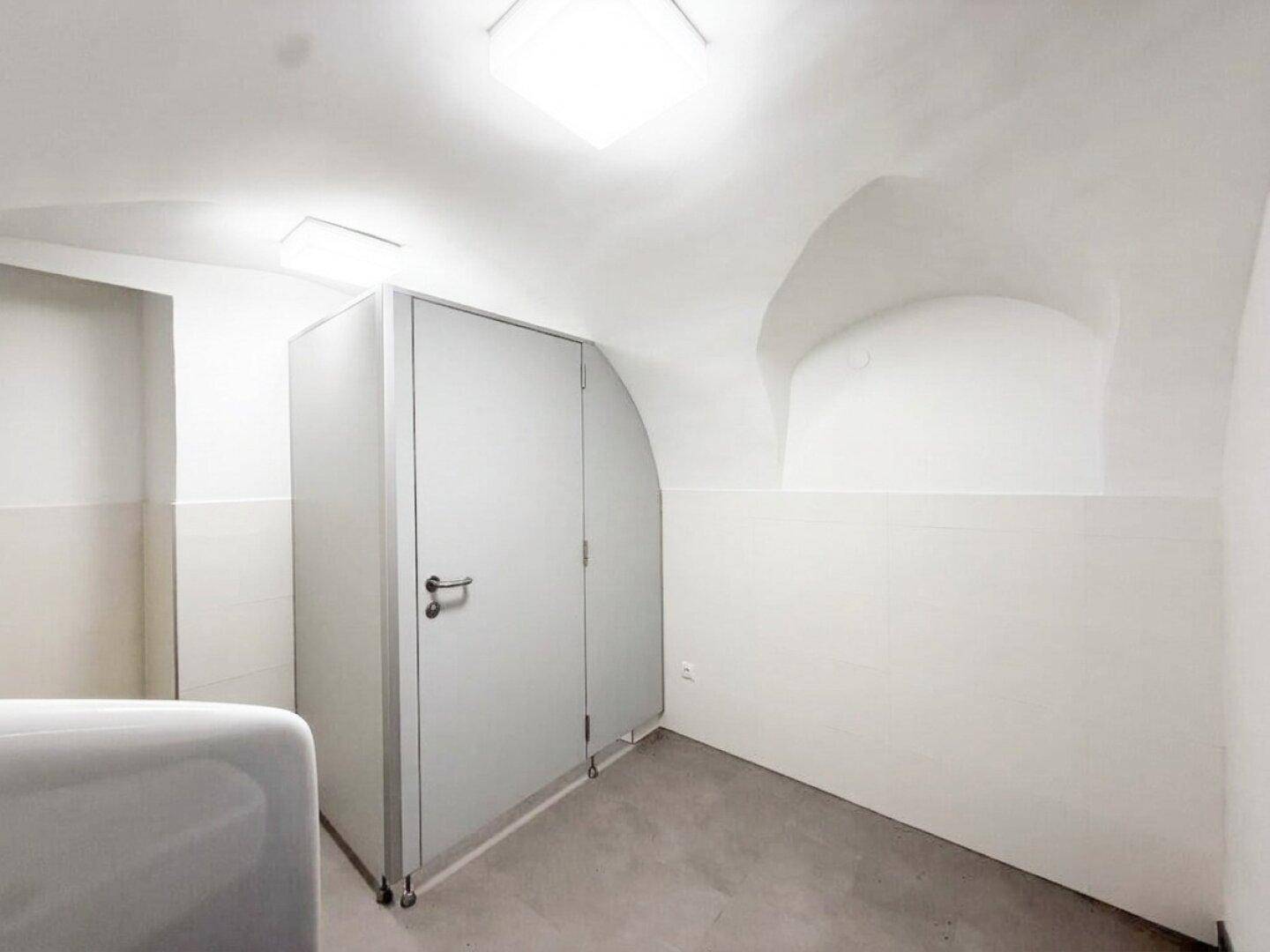 Ansicht der Toilettenkabinen in einem öffentlichen Waschraum mit Gewölbedecke und Fliesenboden.