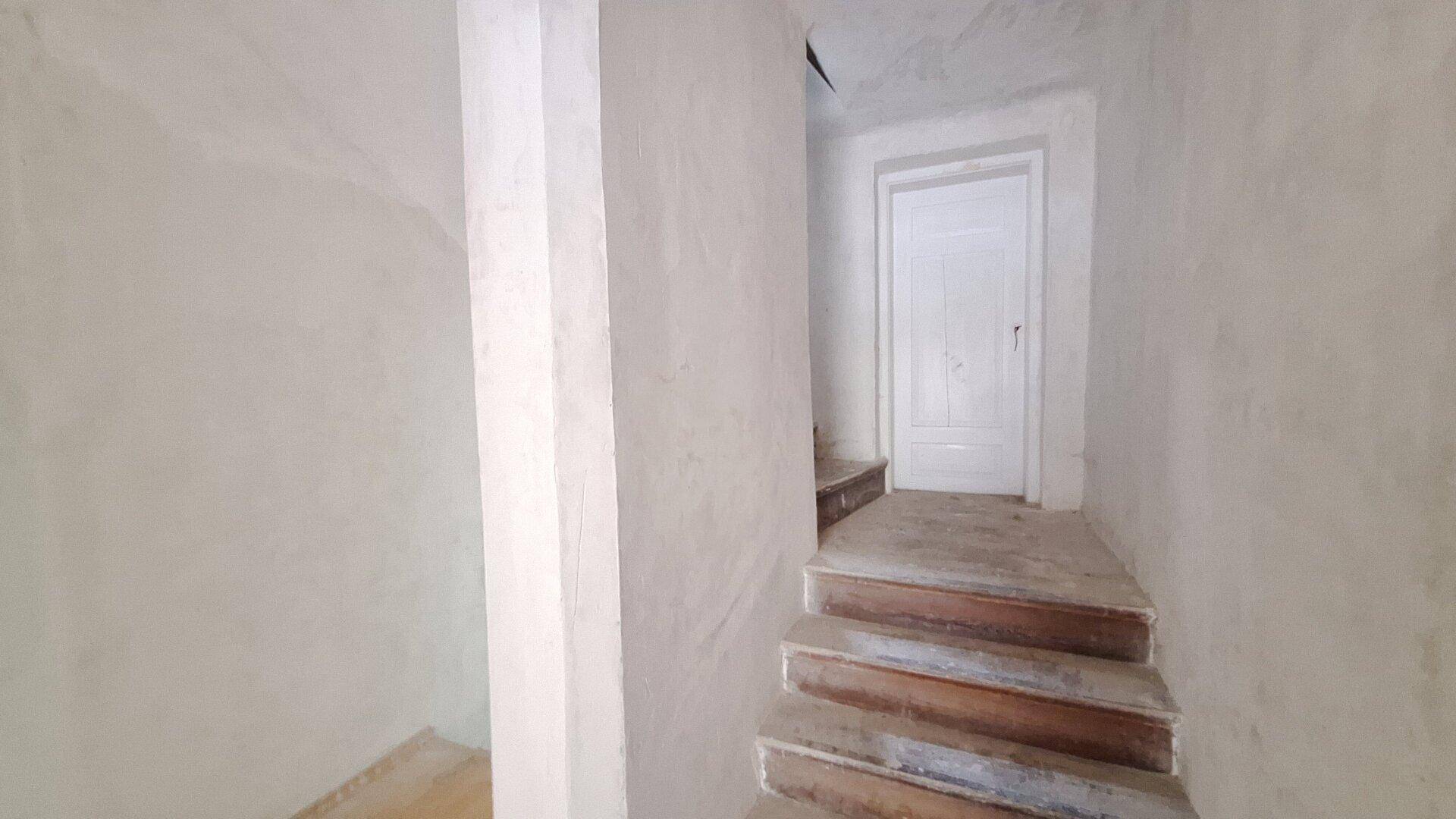 Treppenhaus mit unverputzten Wänden und einer Tür am oberen Ende der Stufen.
