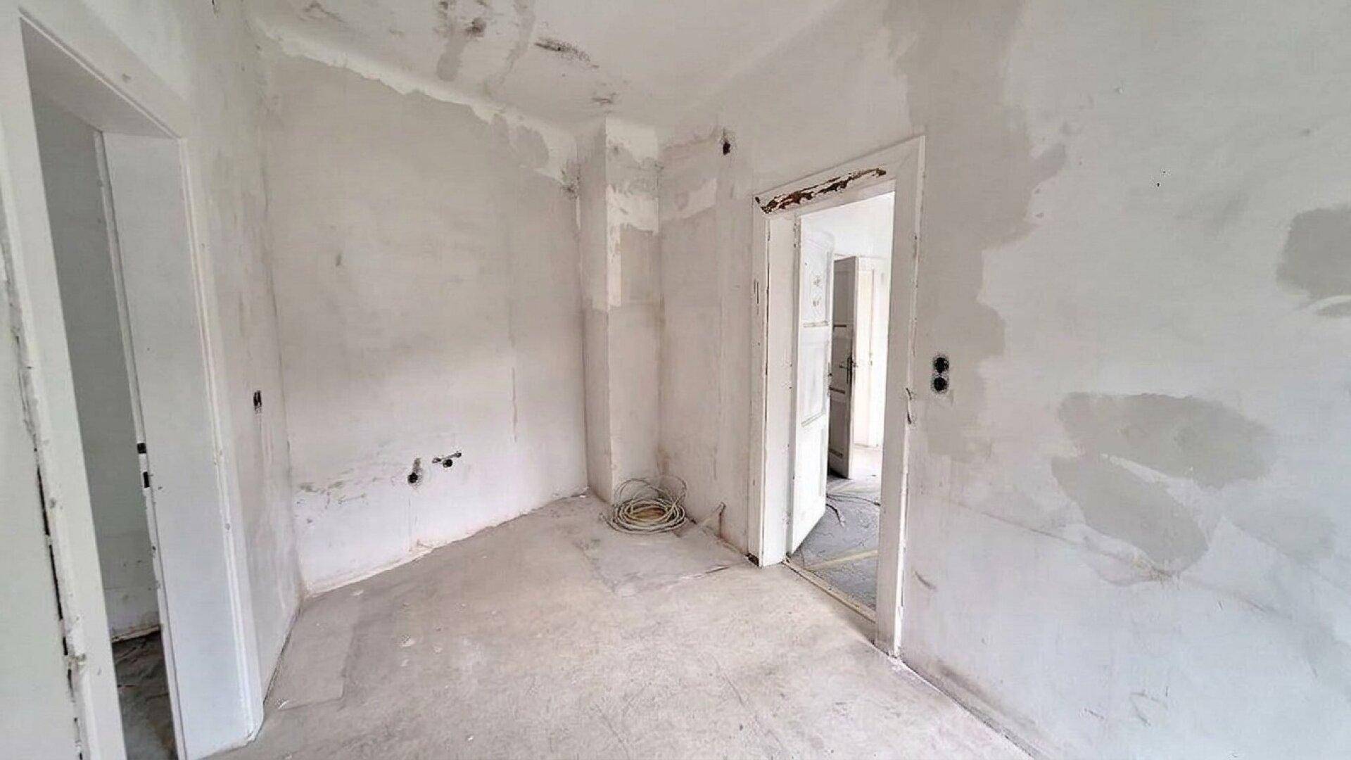 Leerer Raum in Renovierung mit unverputzten Wänden und sichtbaren Installationen.