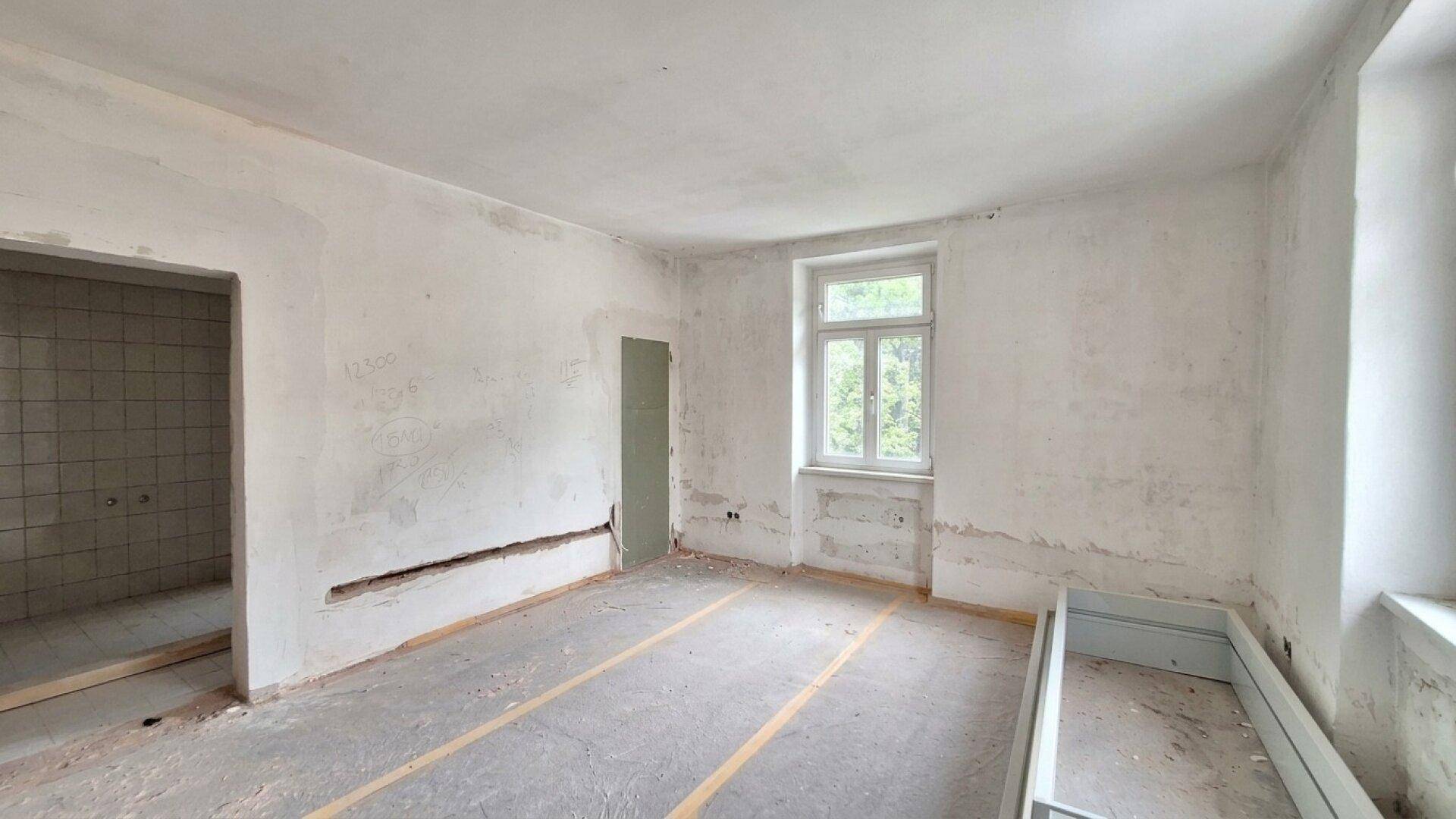 Renovierungsbedürftiger Raum mit einem Fenster und vorbereitetem Boden für neue Beläge.