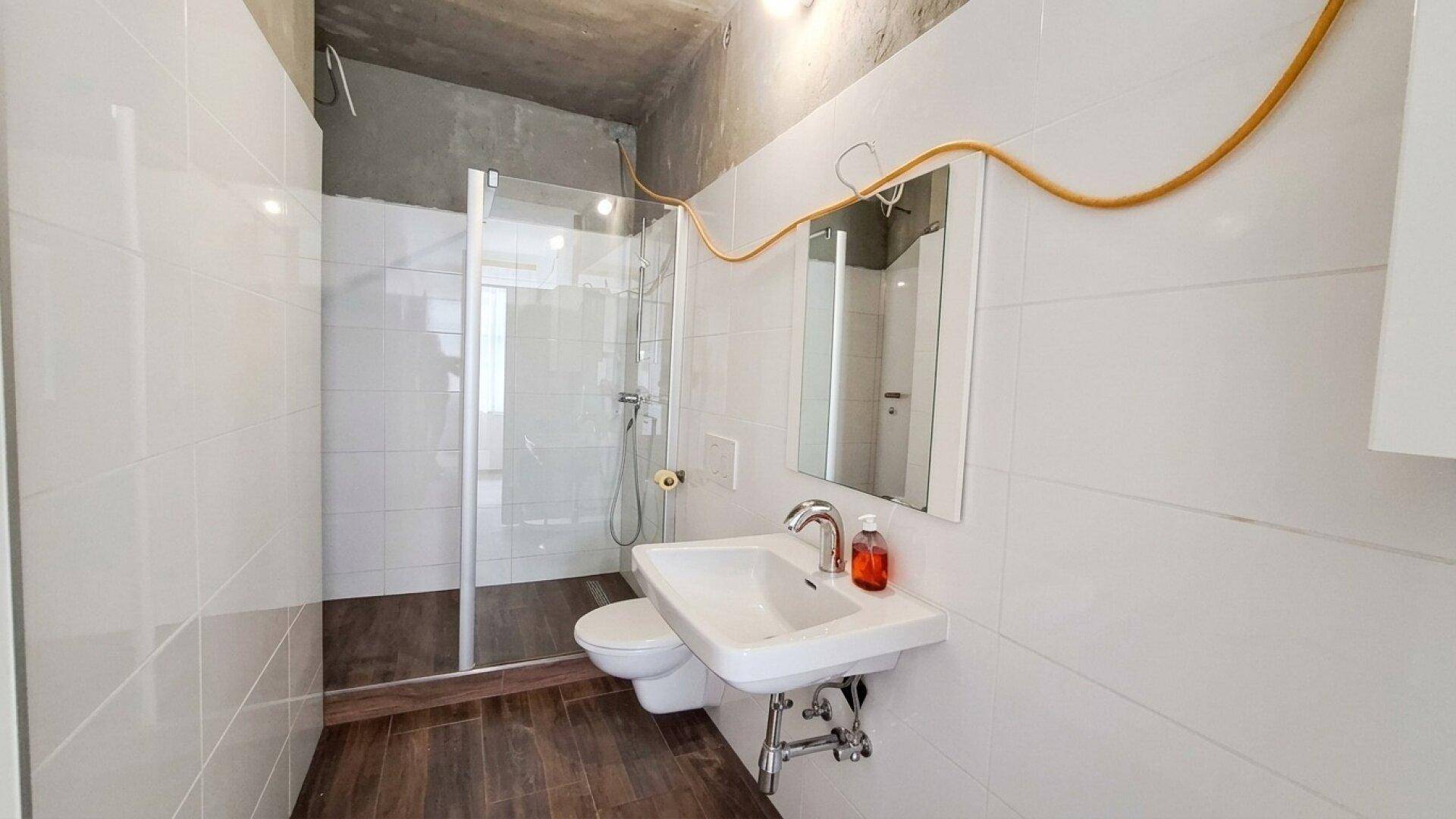 Modernes Badezimmer mit Duschkabine, Waschbecken und Wand-WC, gefliest mit weißen und braunen Fliesen.
