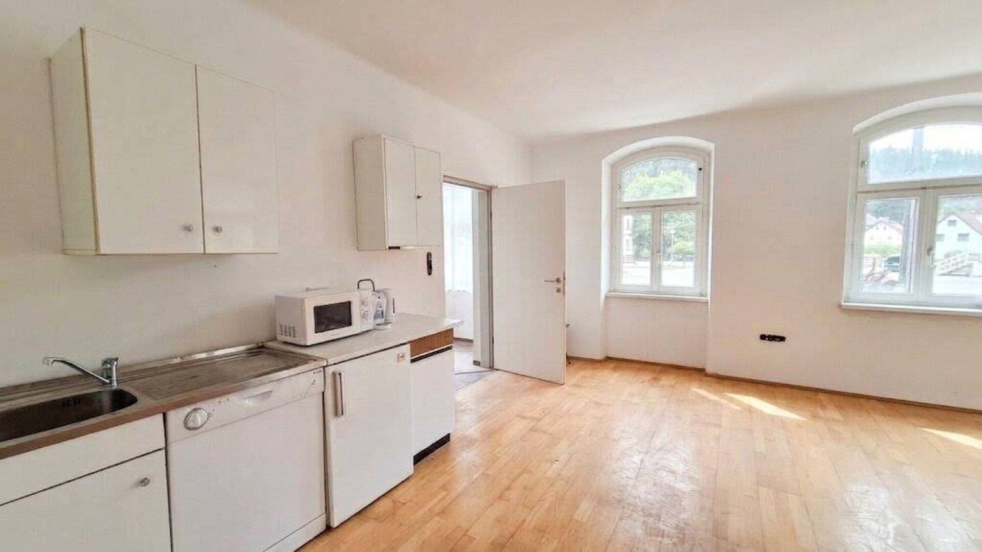 Küchenzeile mit Spüle, Geschirrspüler und Mikrowelle in einem hellen Raum mit Holzboden.