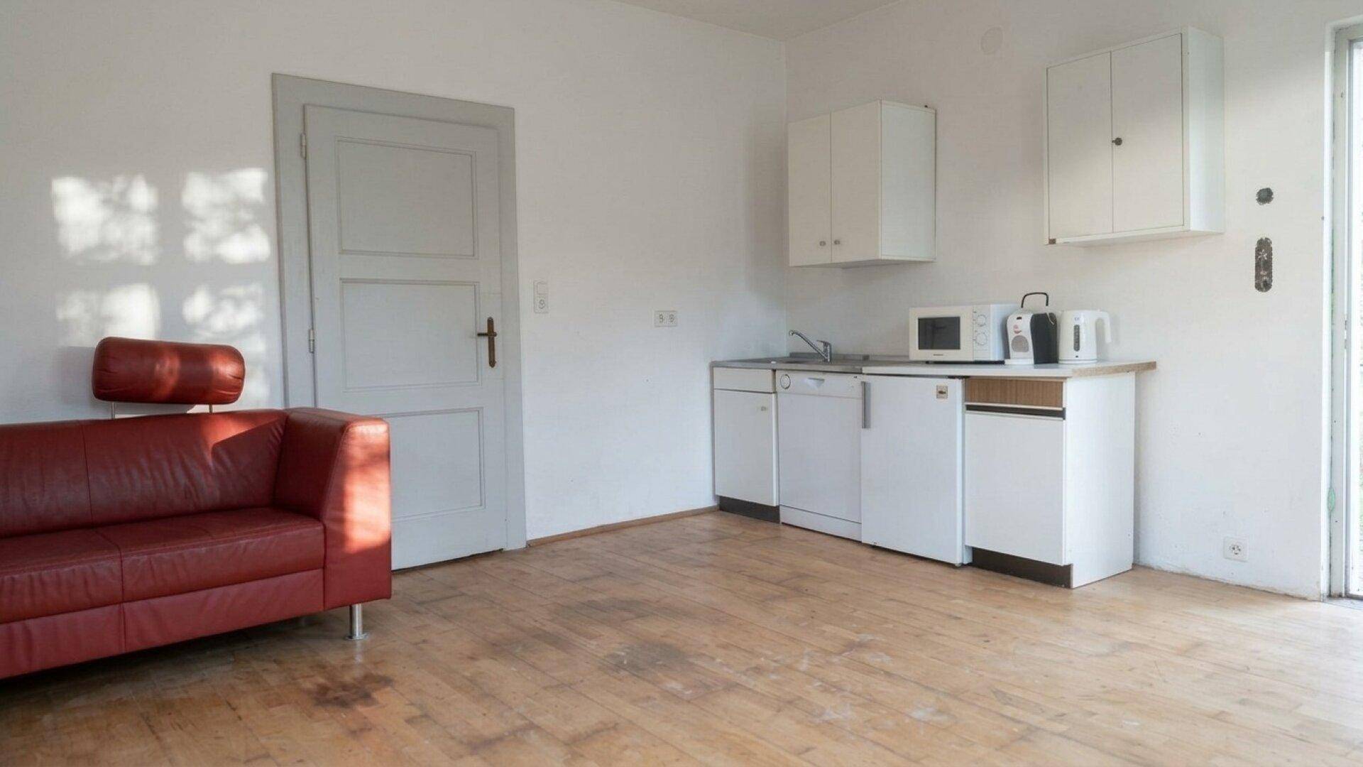 Wohnbereich mit rotem Sofa und einer kleinen Küchenzeile an der Wand.