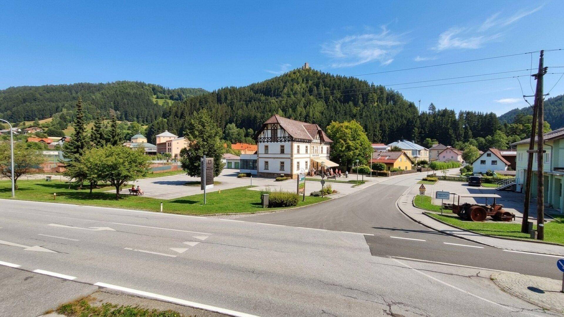 Panoramablick auf eine ländliche Ortschaft mit einem historischen Gebäude und bewaldeten Hügeln.