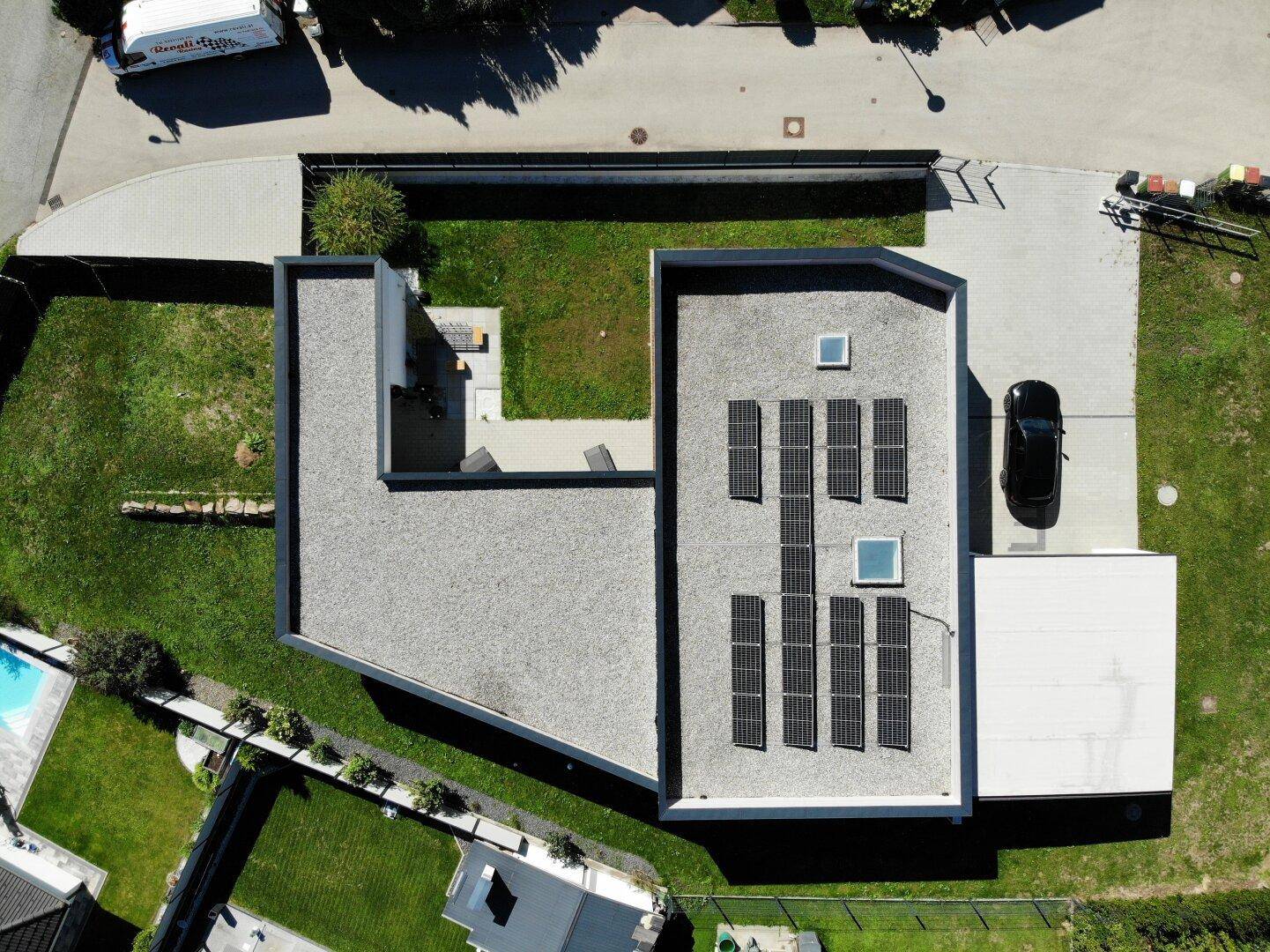 Draufsicht auf das moderne Haus mit Flachdach, Solarpaneelen und großem Gartenbereich.
