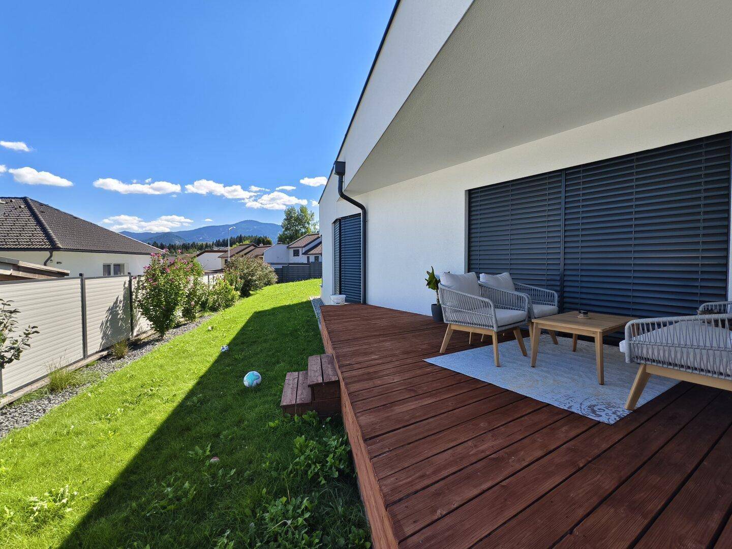 Holzterrasse mit modernen Gartenmöbeln und Blick auf die grüne Umgebung und Berge.