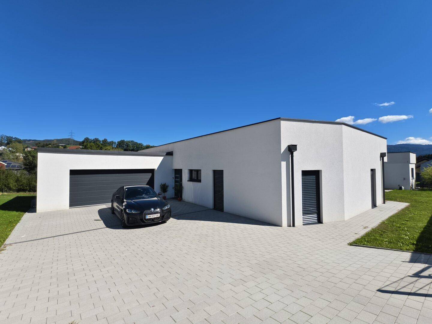 Moderne Hausfassade mit integrierter Garage, gepflasterter Auffahrt und klaren Linien.