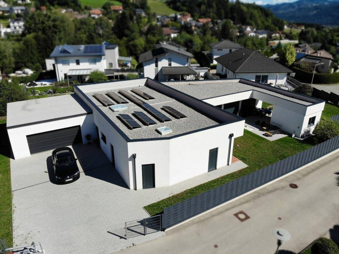 Vogelperspektive eines modernen Hauses mit Garage, gepflasterter Auffahrt und Solarpaneelen auf dem Flachdach.