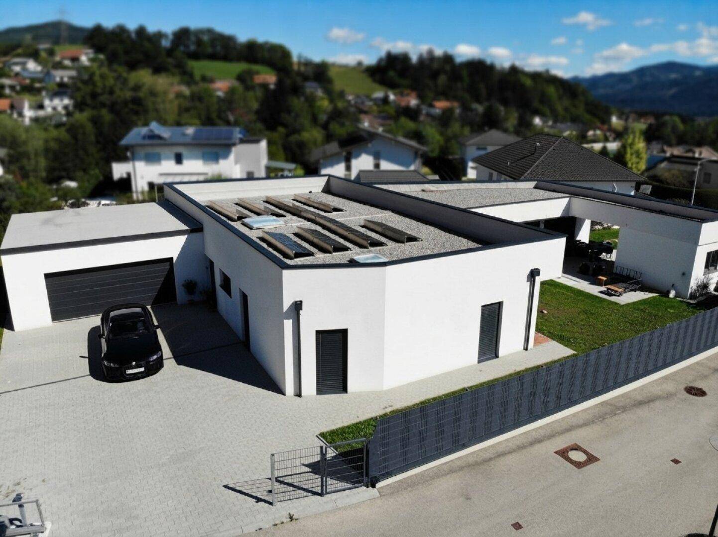 Luftaufnahme des modernen Einfamilienhauses mit Flachdach, Garage und Solaranlage in sonniger Lage.