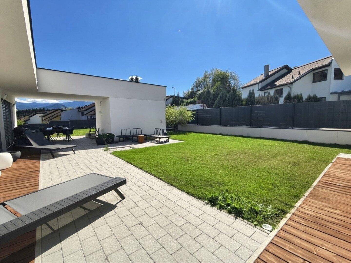 Großer, gepflegter Garten mit Rasenfläche und einer sonnigen Terrasse mit Liegestühlen.