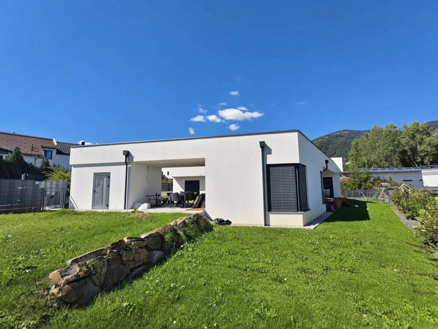 Rückseite des modernen Hauses mit großem Garten, Rasenfläche und einer Steinmauer.