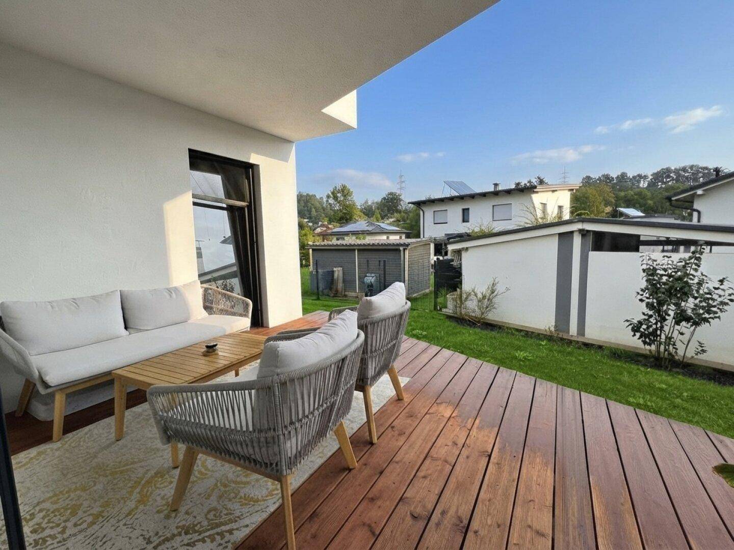 Gemütliche Holzterrasse mit modernen Lounge-Möbeln und Blick auf den Garten und die Umgebung.