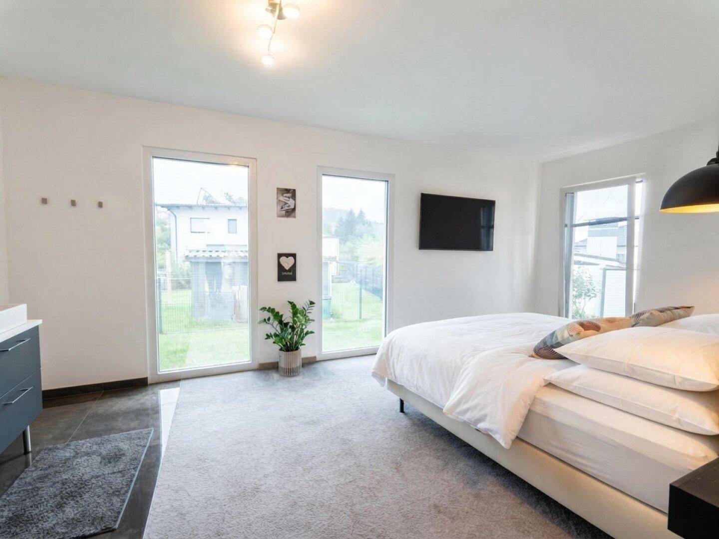 Helles Schlafzimmer mit Teppichboden, großen Fenstern und Blick in den Garten.