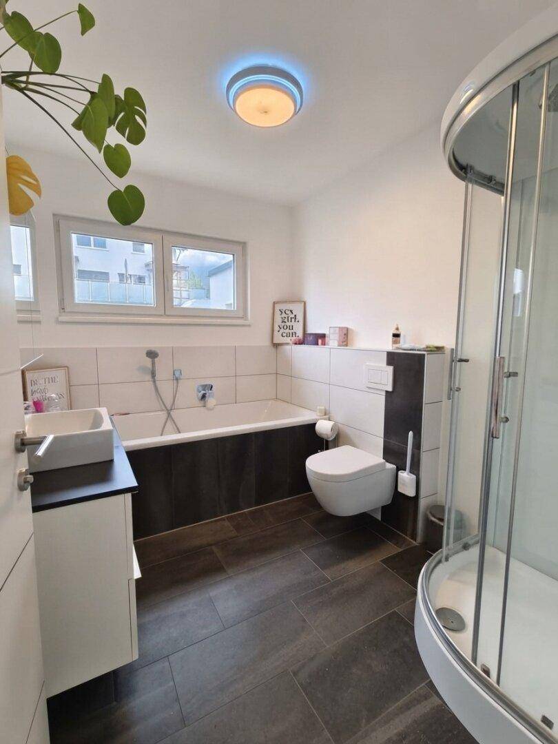 Modernes Badezimmer mit Badewanne, Duschkabine, wandhängendem WC und Fenster.