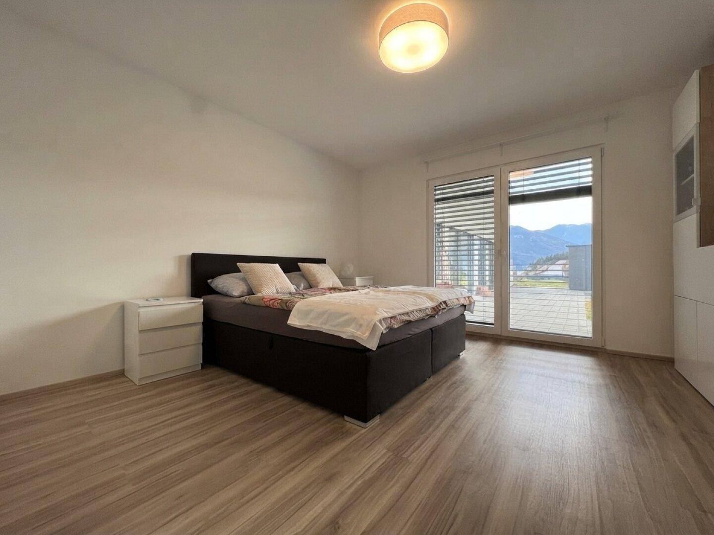 Helles Schlafzimmer mit Doppelbett, Laminatboden und Zugang zu einem Außenbereich.
