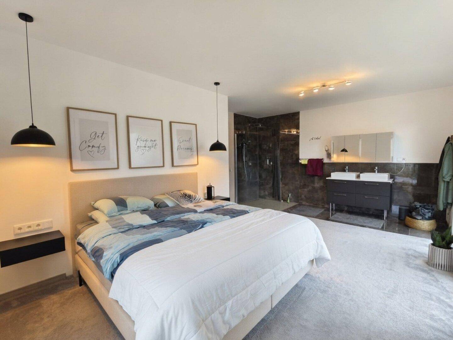 Großes Schlafzimmer mit Teppichboden und offenem Übergang zu einem modernen Badbereich.