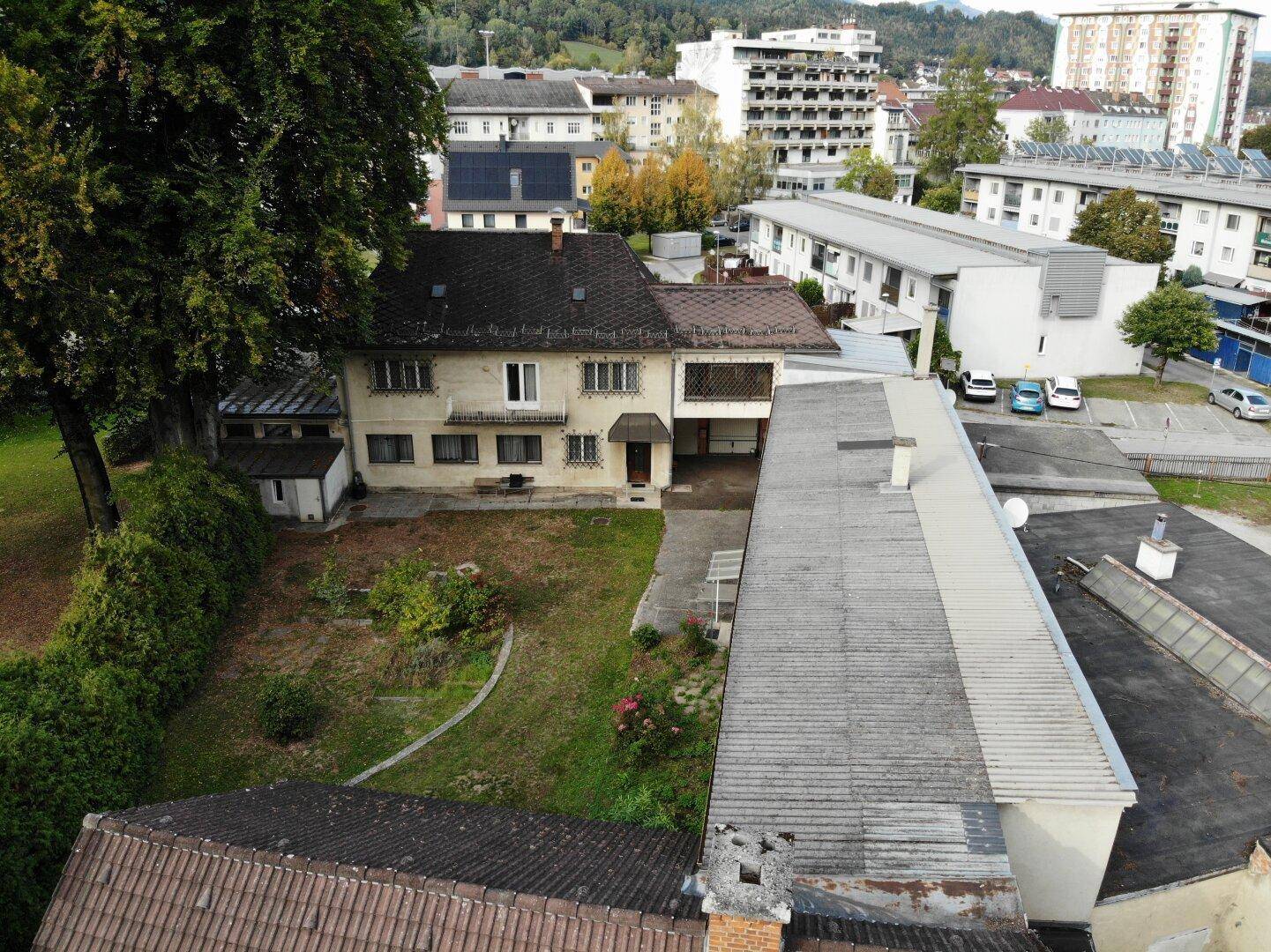 Wohngebäude mit Garten und angrenzendem Flachdachbau, umgeben von städtischer Bebauung.