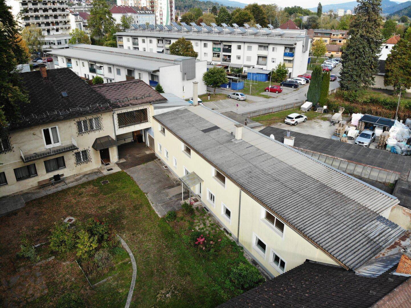 Vogelperspektive eines Wohnhauses mit Garten und einem langen Anbau, im städtischen Umfeld.