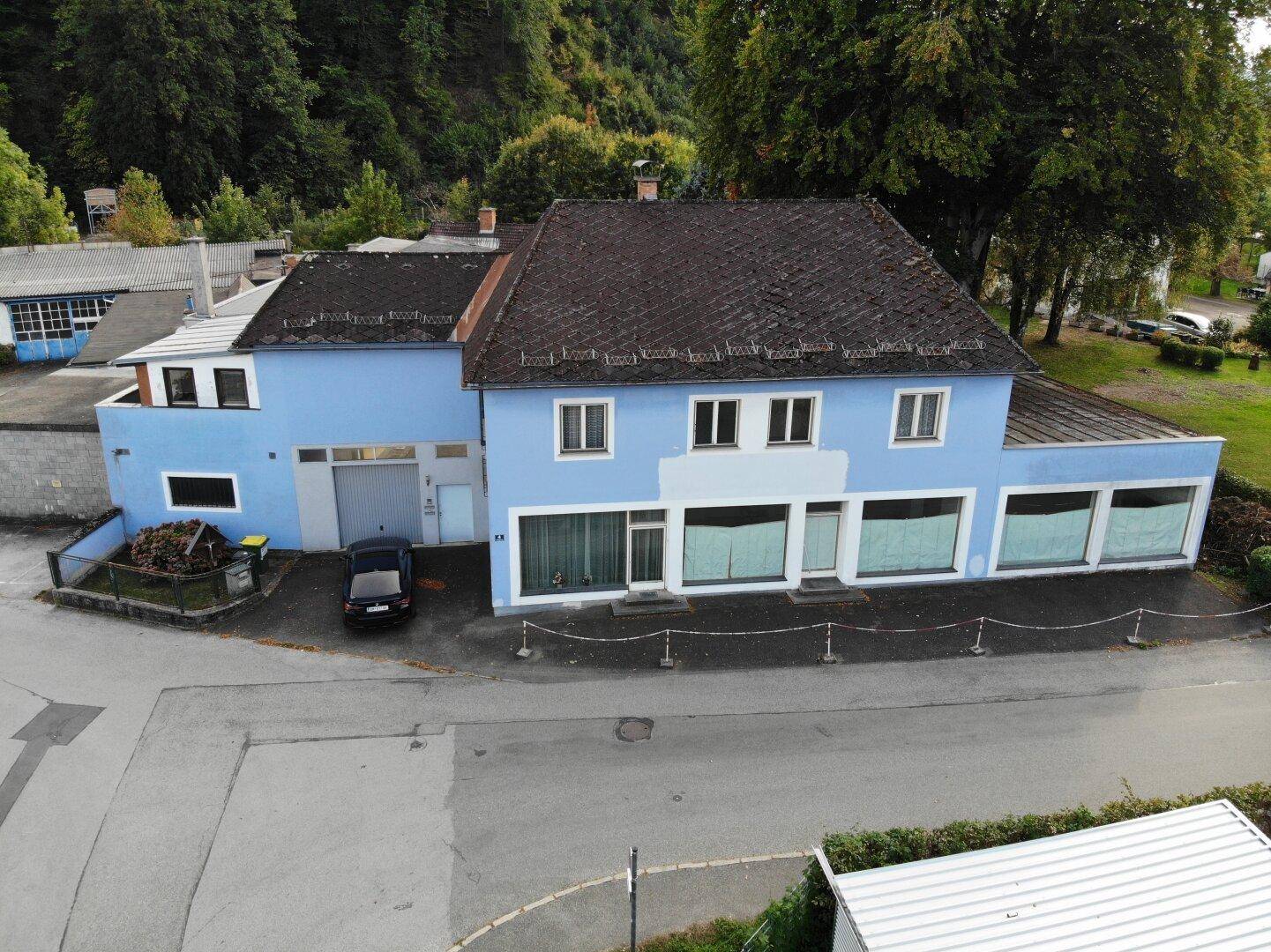 Vogelperspektive des blauen Gebäudekomplexes mit dunklem Dach und angrenzenden Flächen.
