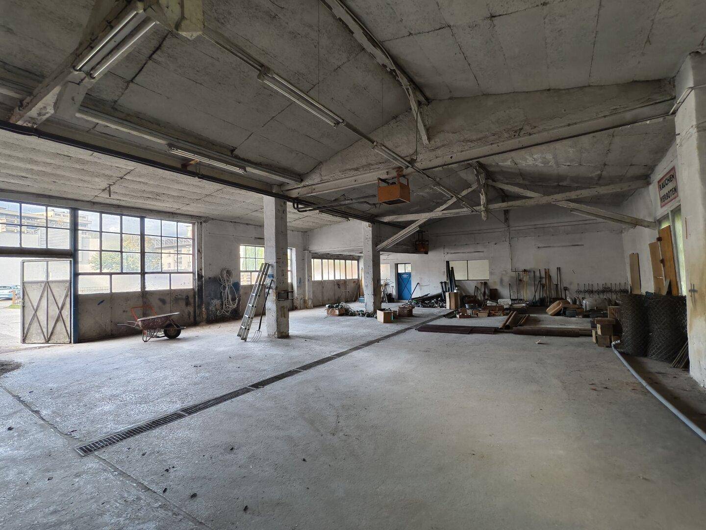 Großer, leerer Industrieraum mit Betonboden, hohen Decken und großen Fenstern.
