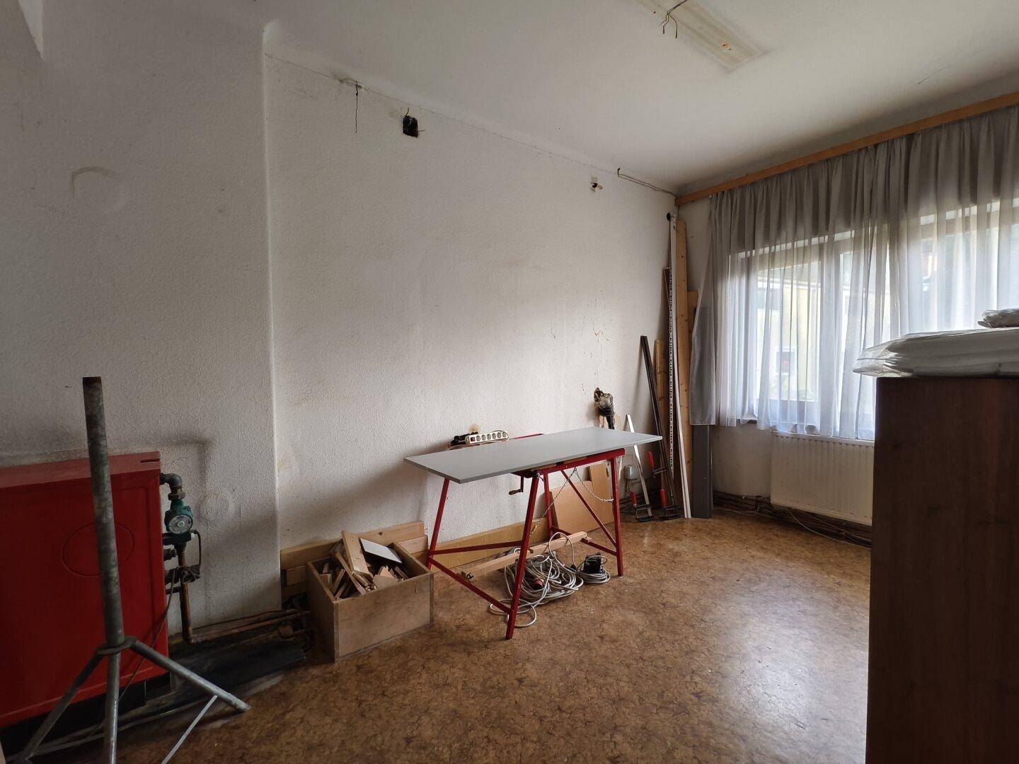 Raum mit Fenster, Vorhängen und einem Tisch, der Boden ist gemustert.