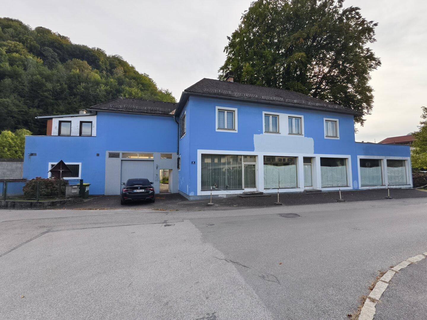 Straßenansicht des blauen Gebäudes mit großen Schaufenstern und einer Garageneinfahrt.
