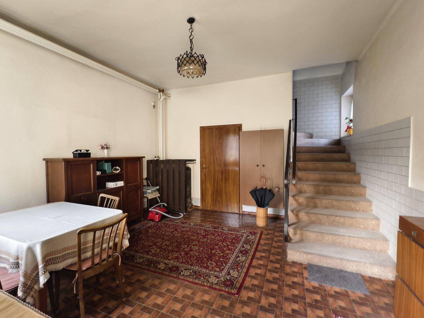 Esszimmer mit Holztisch, Stühlen, Teppich und Holzschrank, mit Treppenaufgang.