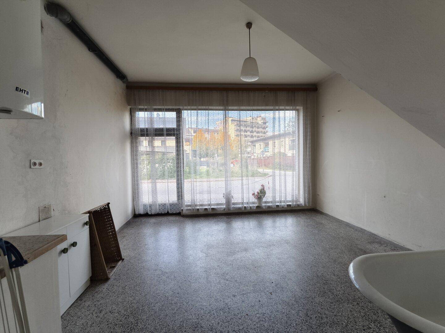 Heller Raum mit großer Fensterfront, Küchenzeile und Badewanne, der Renovierungsbedarf aufweist.