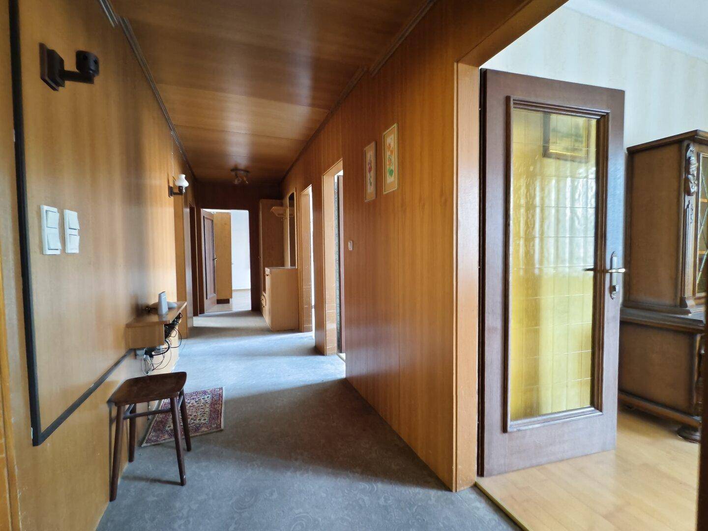 Langer Flur mit Holzvertäfelung an Wänden und Decke, der zu mehreren Zimmern führt.