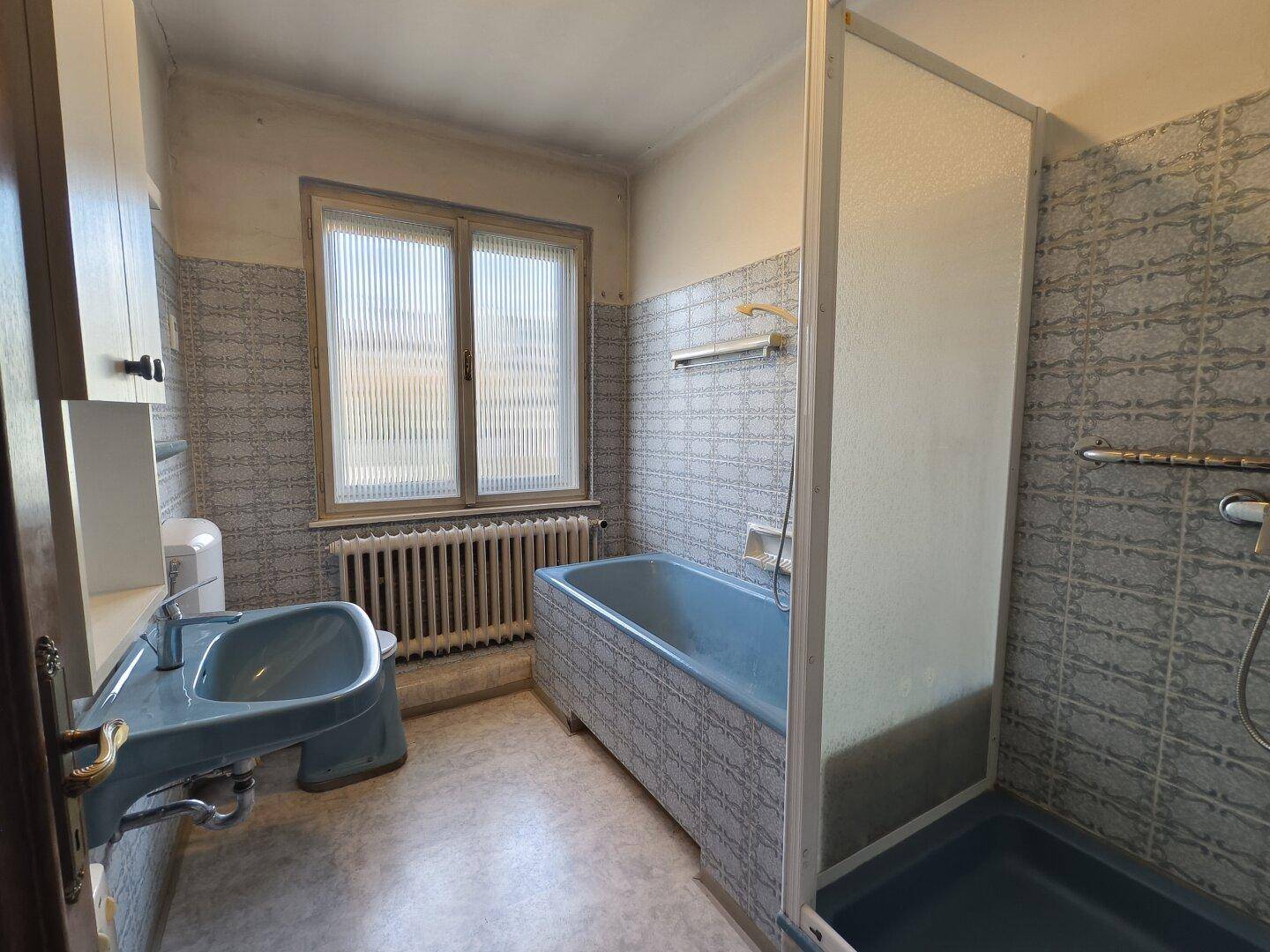 Badezimmer im Stil der 80er Jahre mit blauen Sanitärobjekten, Fliesen und Duschkabine.