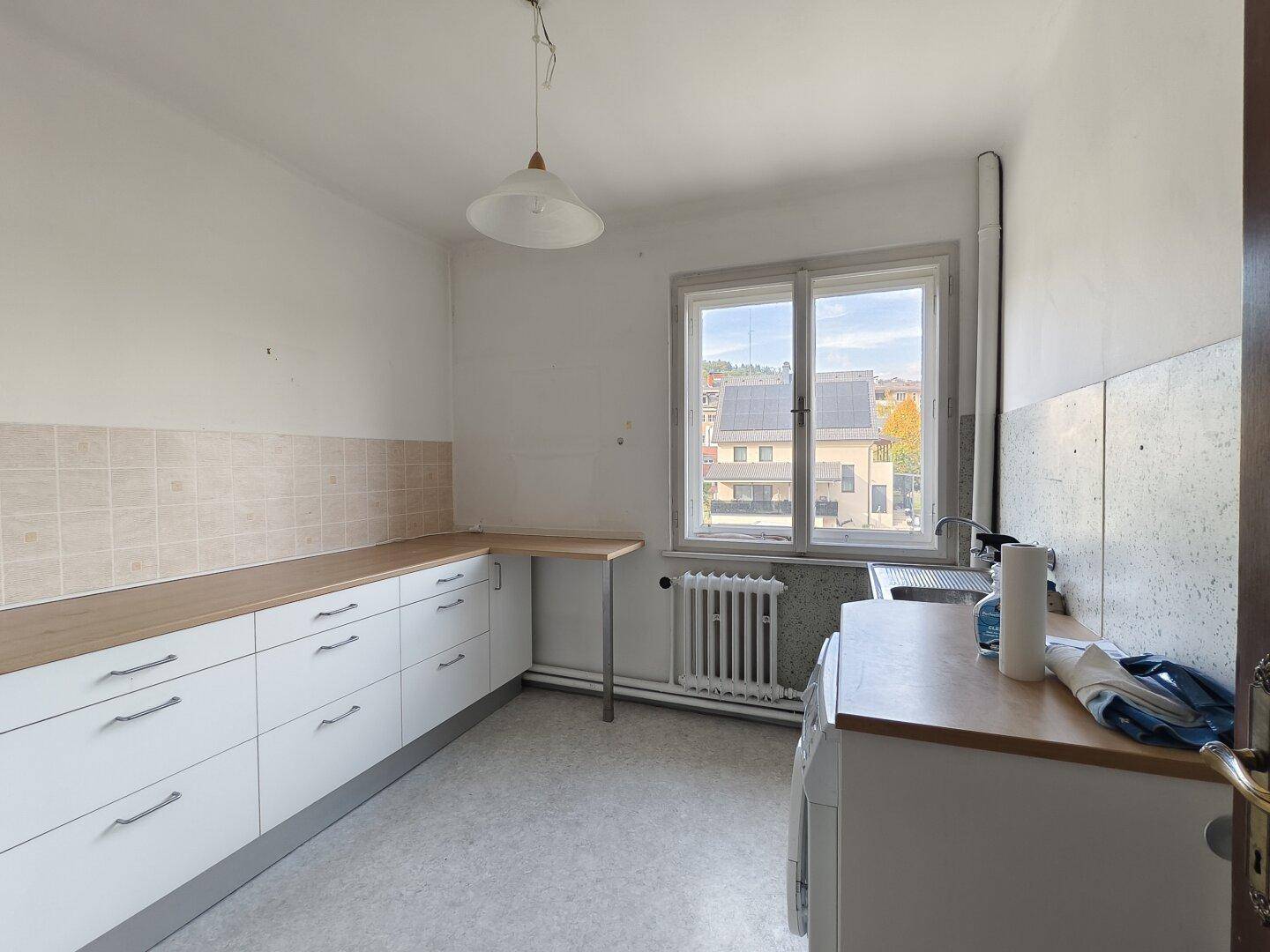 Helle Küche mit weißen Unterschränken, Holz-Arbeitsplatte und Fenster mit Ausblick.