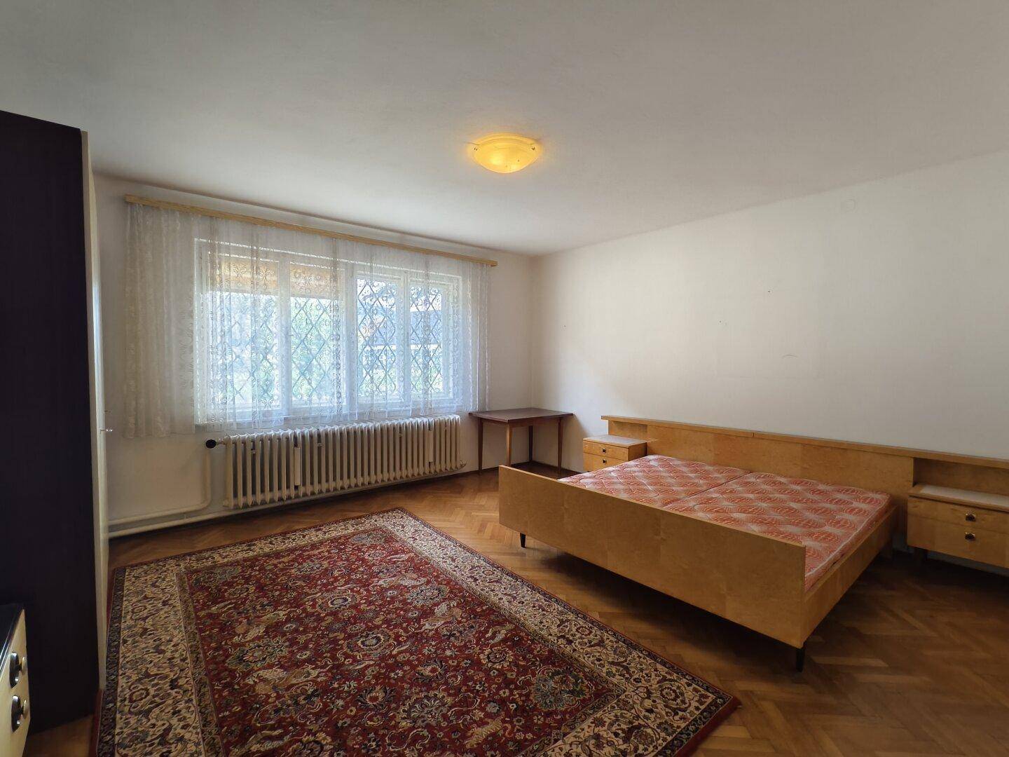 Schlafzimmer mit Holzparkett, großem Bett und Nachttischen, beleuchtet durch ein Fenster.