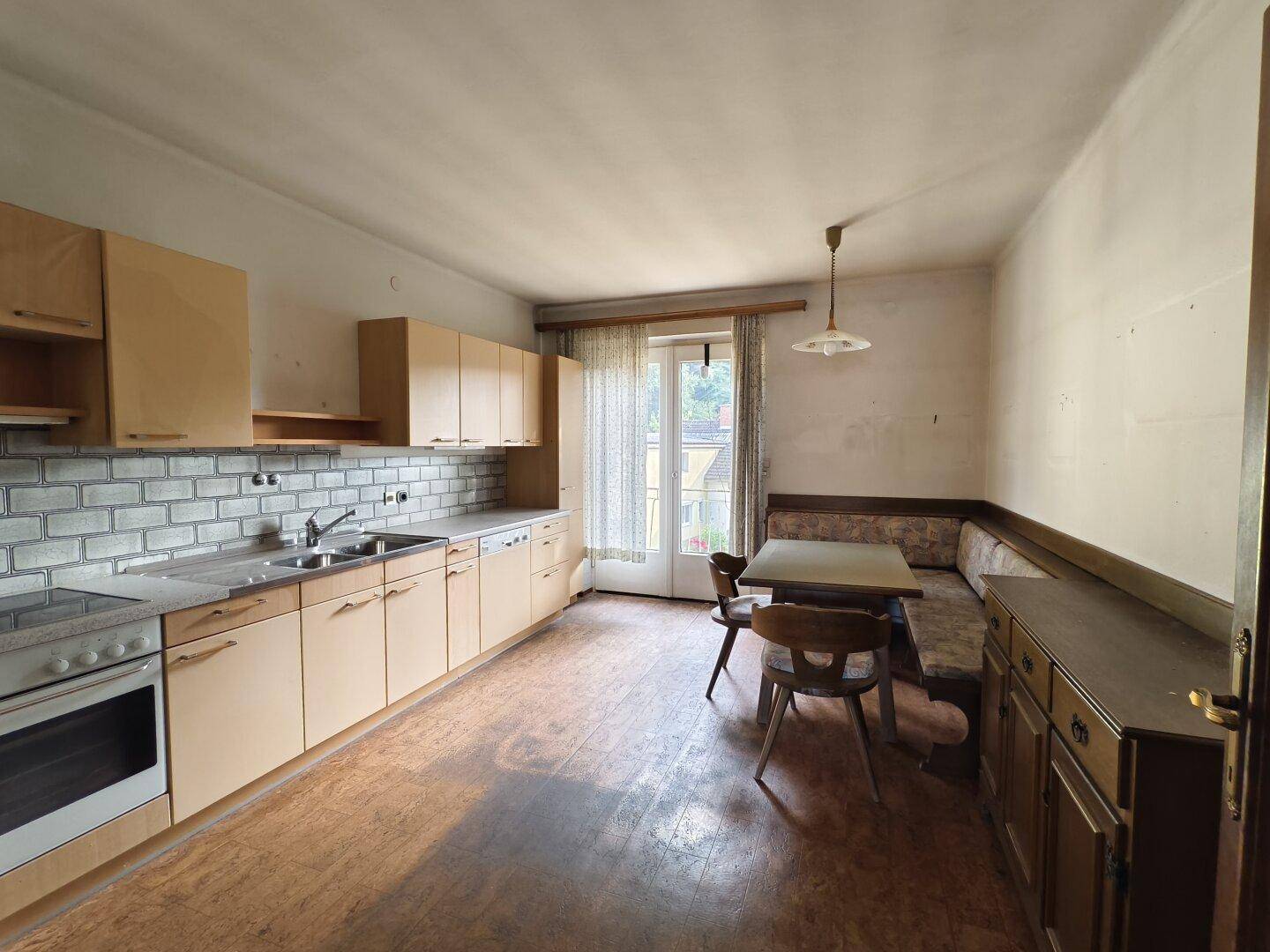 Wohnküche mit hellen Holzschränken, Essecke und Zugang zu einem kleinen Balkon.
