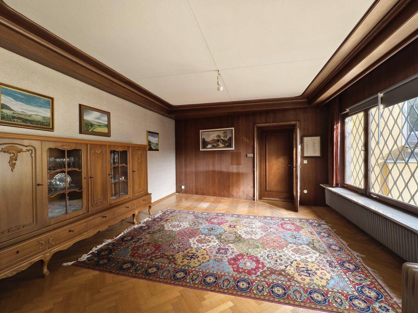 Elegantes Wohnzimmer mit Holzvertäfelung, Parkettboden und einem farbenfrohen Orientteppich.