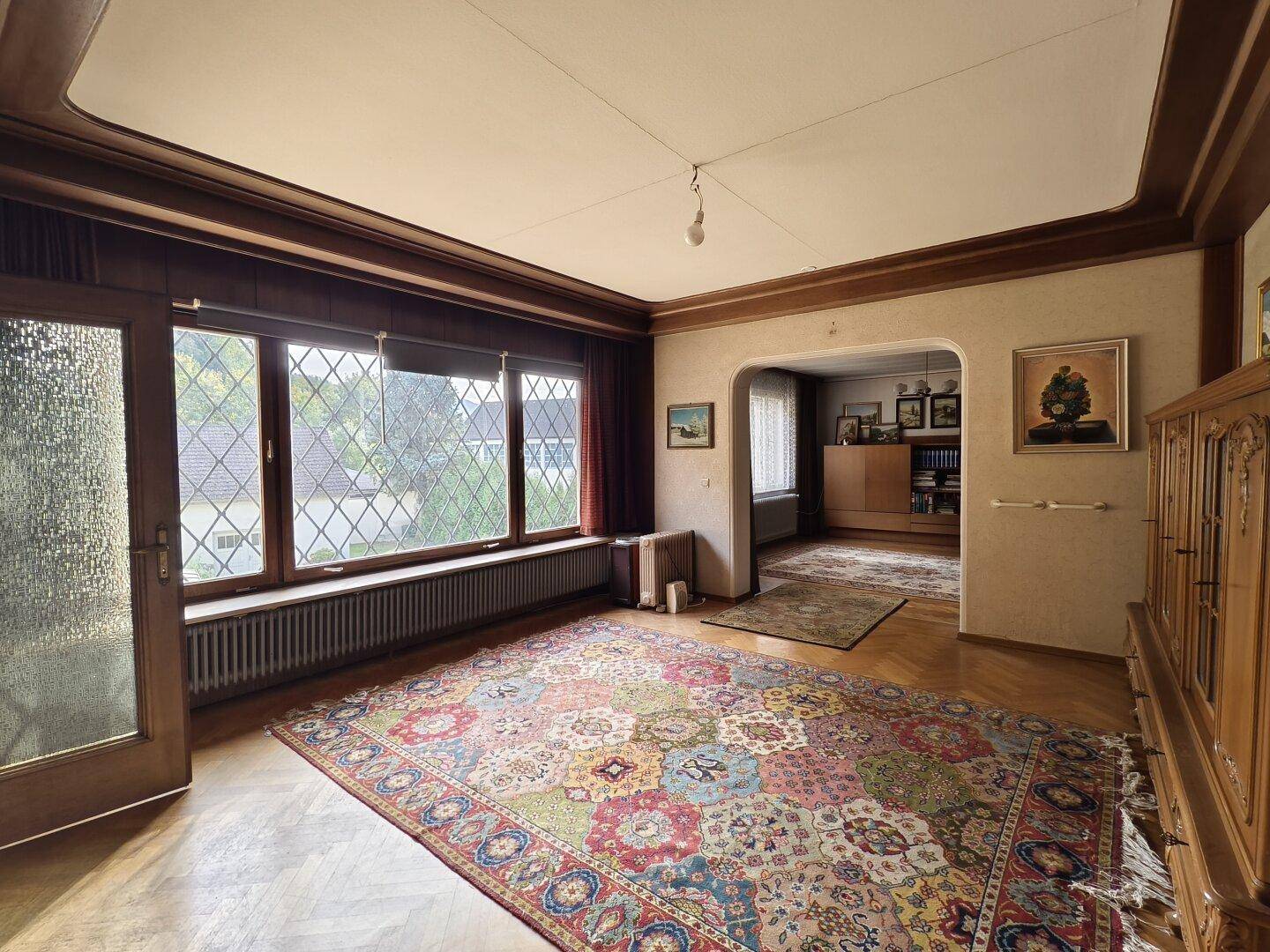 Großzügiges Wohnzimmer mit Holzvertäfelung, Parkettboden und farbenfrohem Teppich.