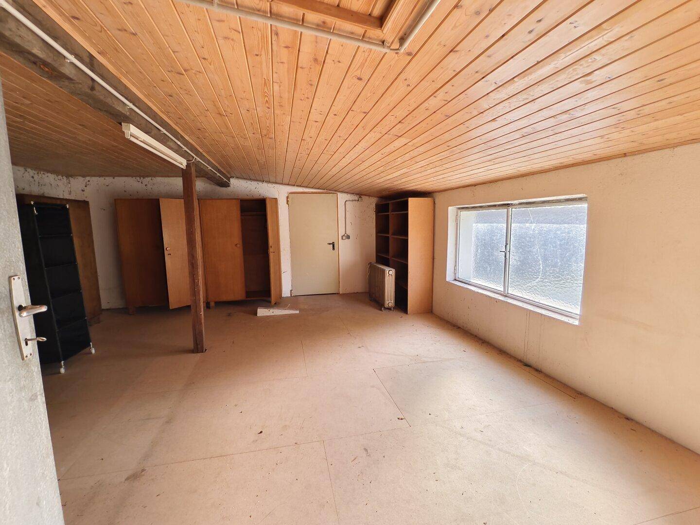 Geräumiger Mehrzweckraum mit Holzdecke, Betonboden und Fenster.