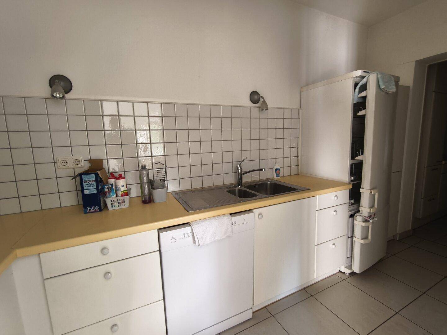 Funktionale Küche mit weißen Schränken, gelber Arbeitsplatte und weißem Fliesenspiegel.
