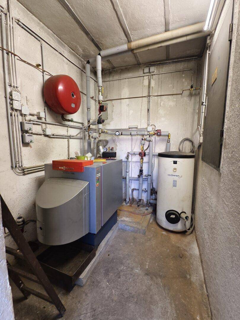 Heizungsraum mit moderner Heizungsanlage, Warmwasserspeicher und sichtbaren Rohrleitungen.