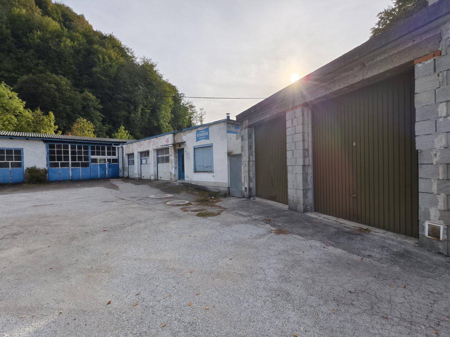 Gebäudekomplex mit Garagentoren und großem Vorplatz vor einer bewaldeten Landschaft.