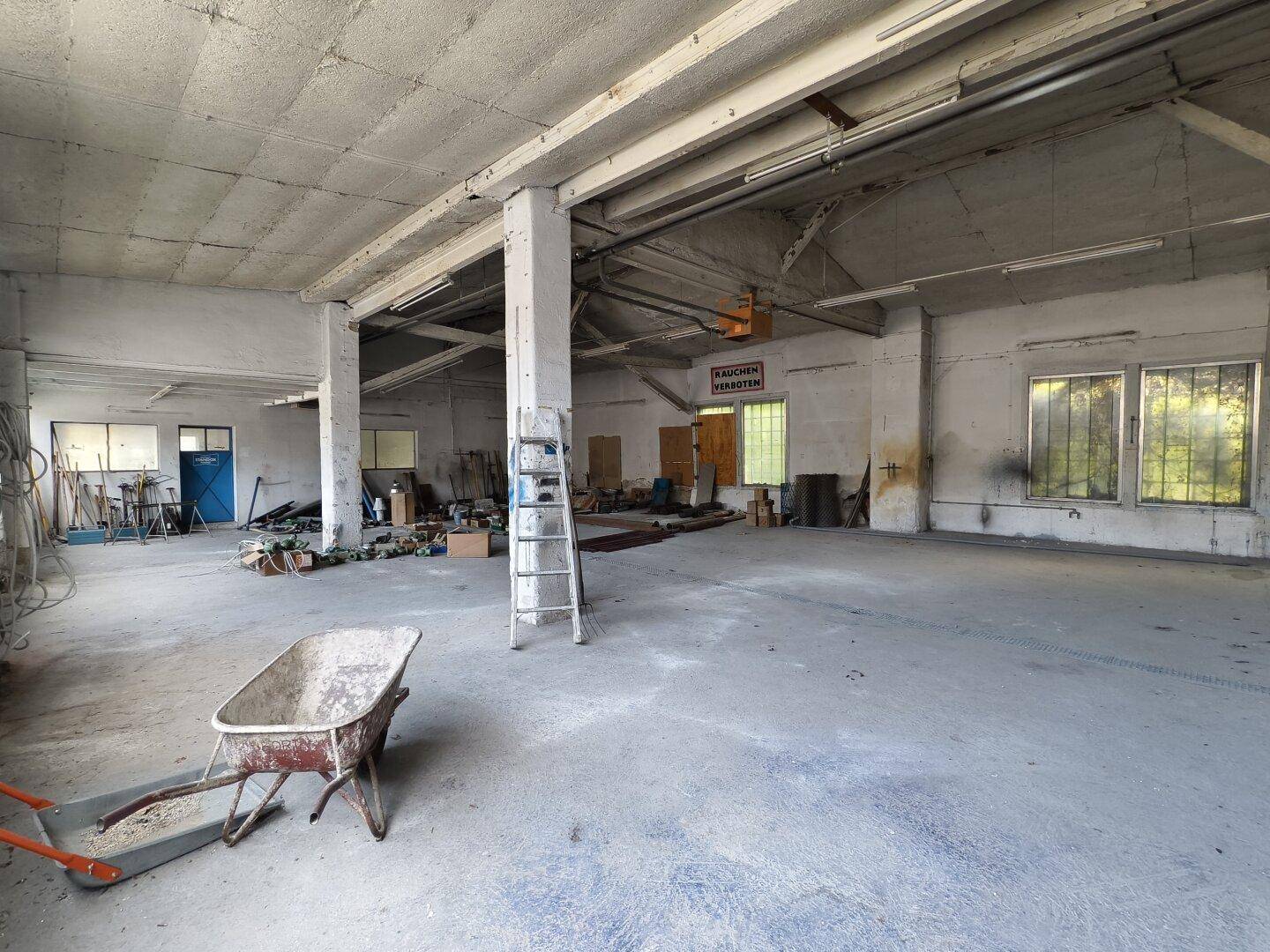Große, leere Industriehalle mit Betonboden, Säulen und Fenstern, bereit zur Nutzung.