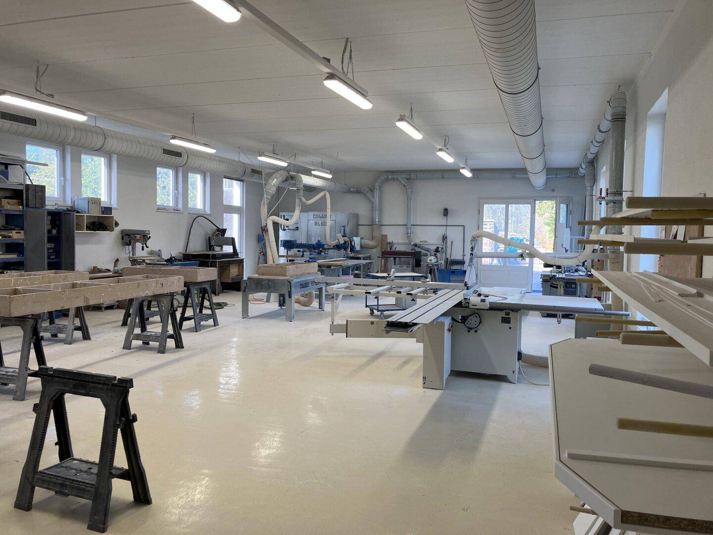 Geräumige Werkstatt mit verschiedenen Holzbearbeitungsmaschinen, Werkbänken und heller Beleuchtung.